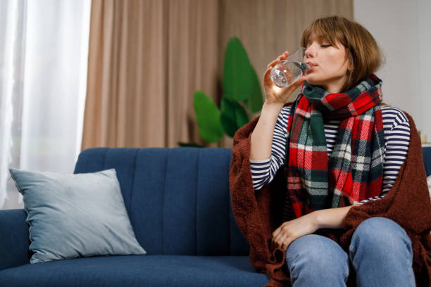 Woman drinking water while sitting on a couch wearing a scarf.